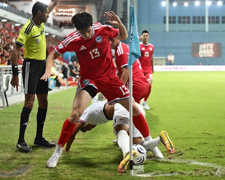Harhys Stewart, wearing 13, shields the ball from a Thailand player by the corner flag at Jalan Besar Stadium as the assistant referee watches